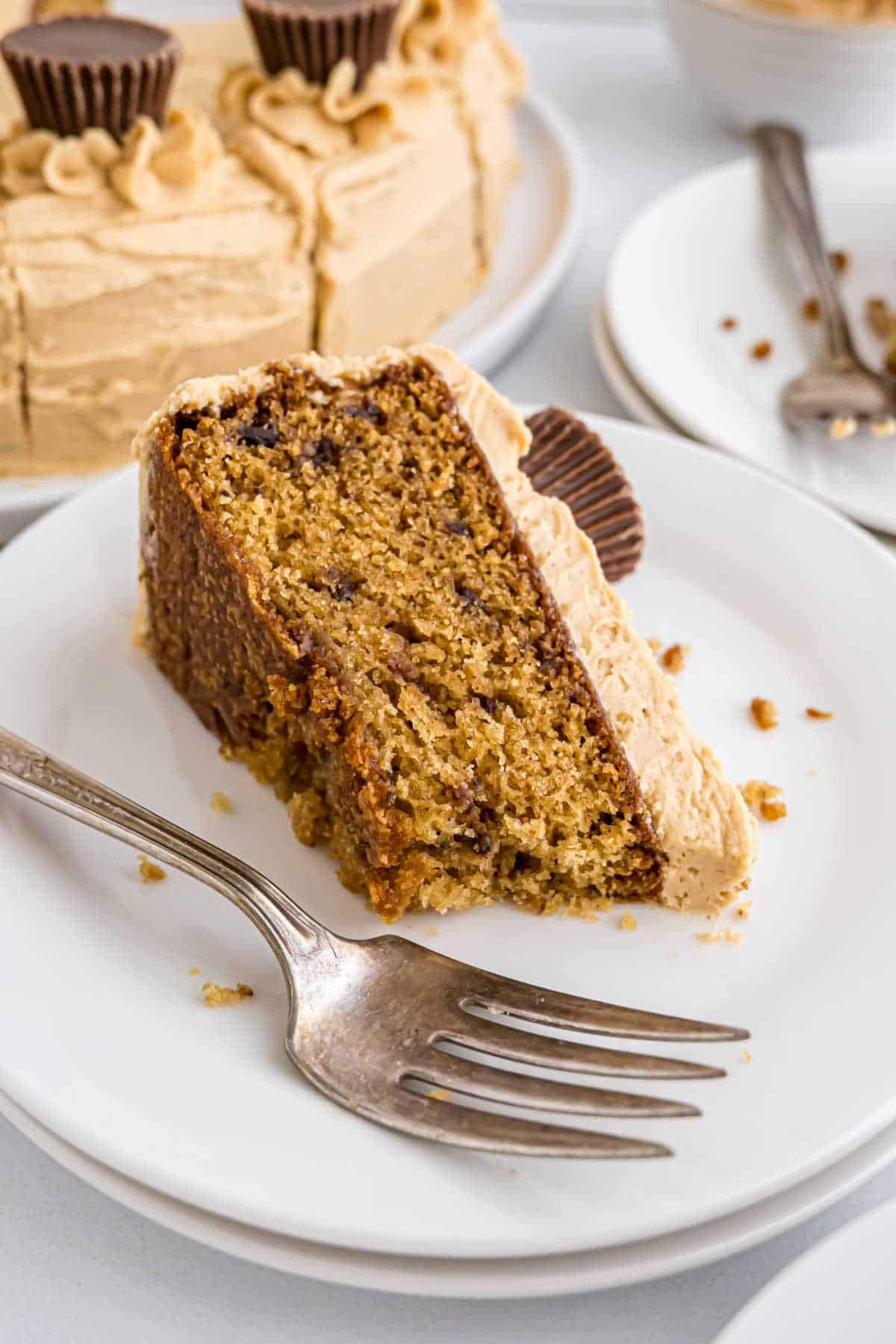 A slice of Reese's peanut butter cake with frosting and a mini peanut butter cup on a white plate with a fork.