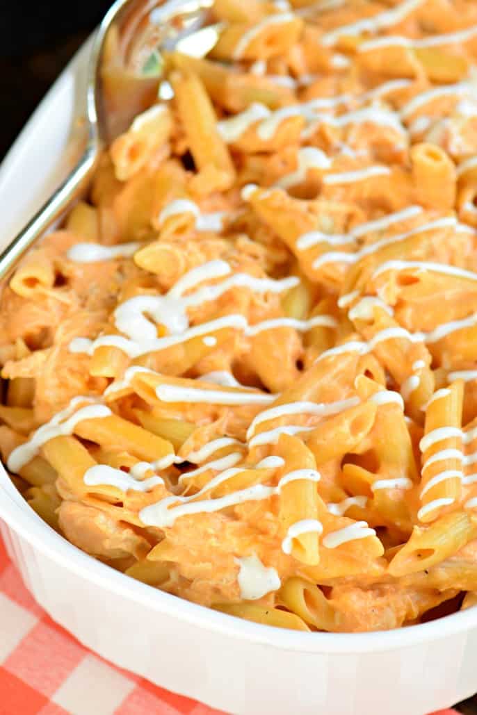 Buffalo chicken pasta in a white casserole dish topped with ranch dressing.