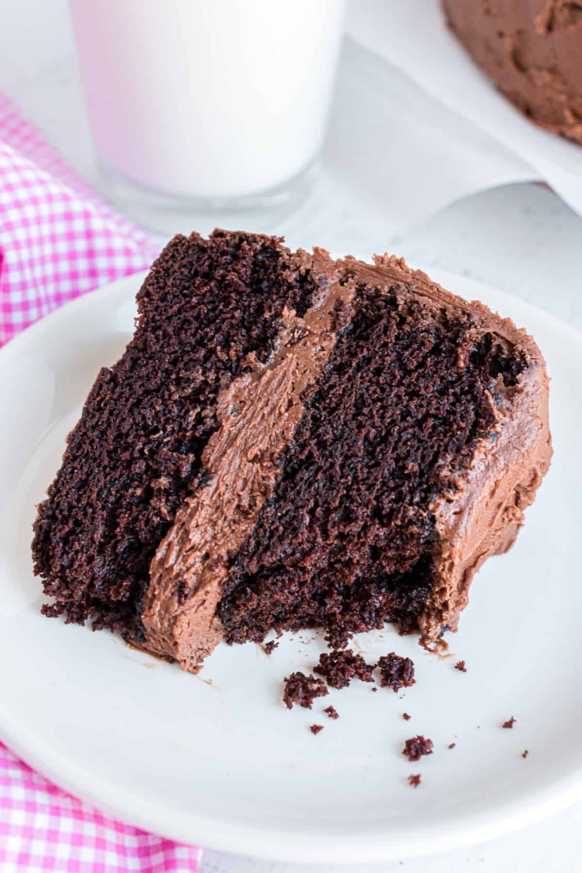 Slice of chocolate layer cake on a white plate with a bite removed and soft crumbs exposed.