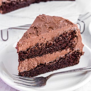 Double layer chocolate cake with chocolate frosting on a white plate.