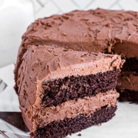 Slice of chocolate layer cake being removed from cake plate with a spatula.