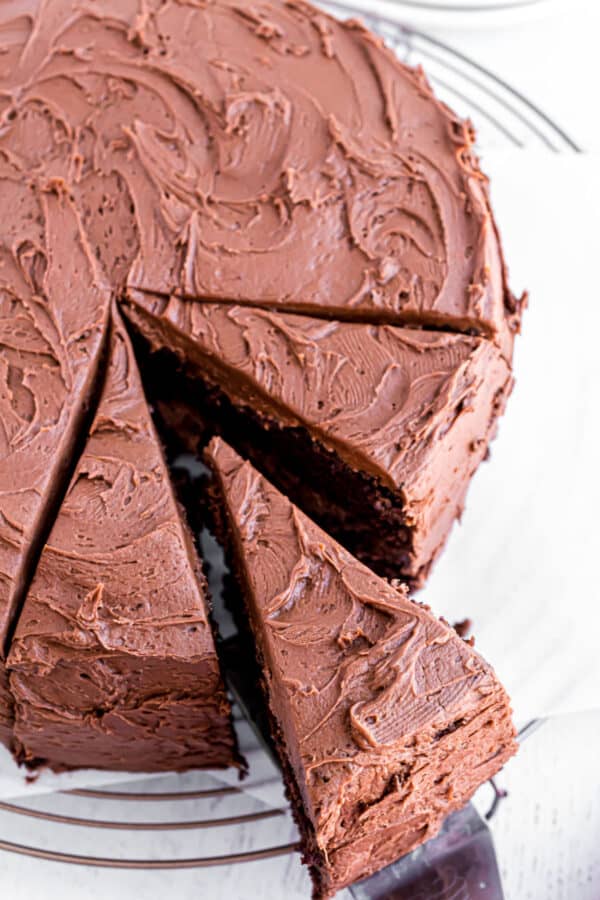 Whole chocolate layer cake with three slices cut and one being removed with a spatula.