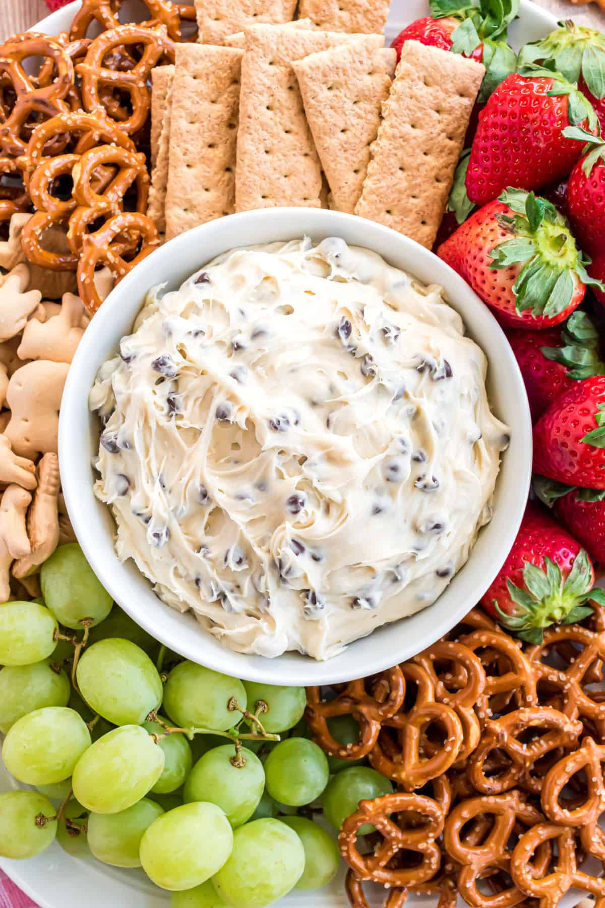 Cookie dough dip in a bowl served with fruit and pretzels.