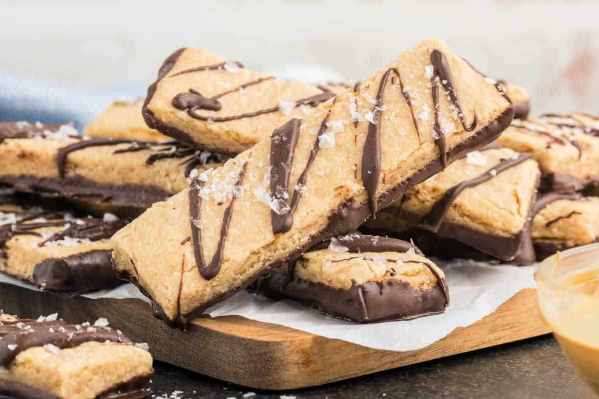 Dark chocolate peanut butter shortbread cookies dipped in chocolate, drizzled with more chocolate, and topped with sea salt on a wooden board.