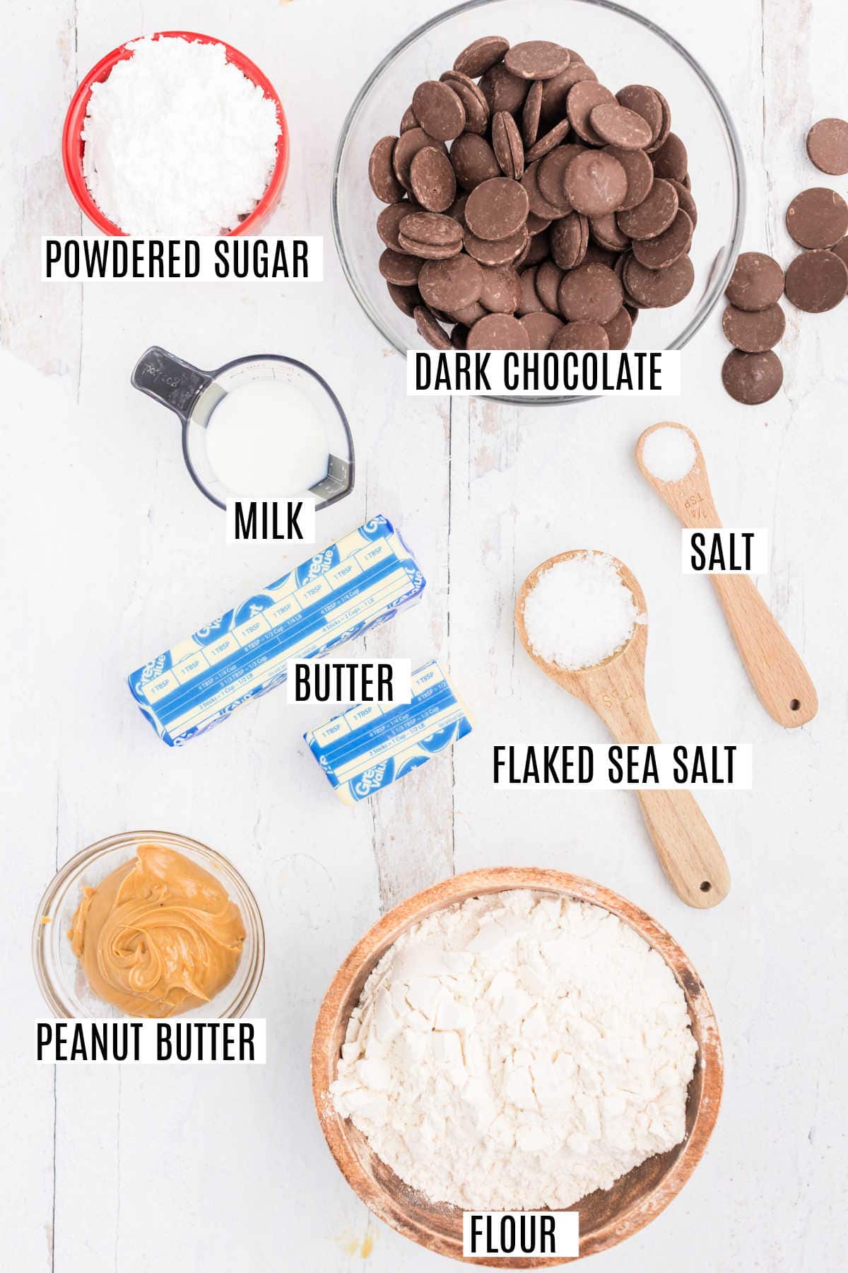 Baking ingredients on a white surface, including chocolate, peanut butter, flour, milk, butter, and sugar—perfect for making dark chocolate peanut butter shortbread cookies.