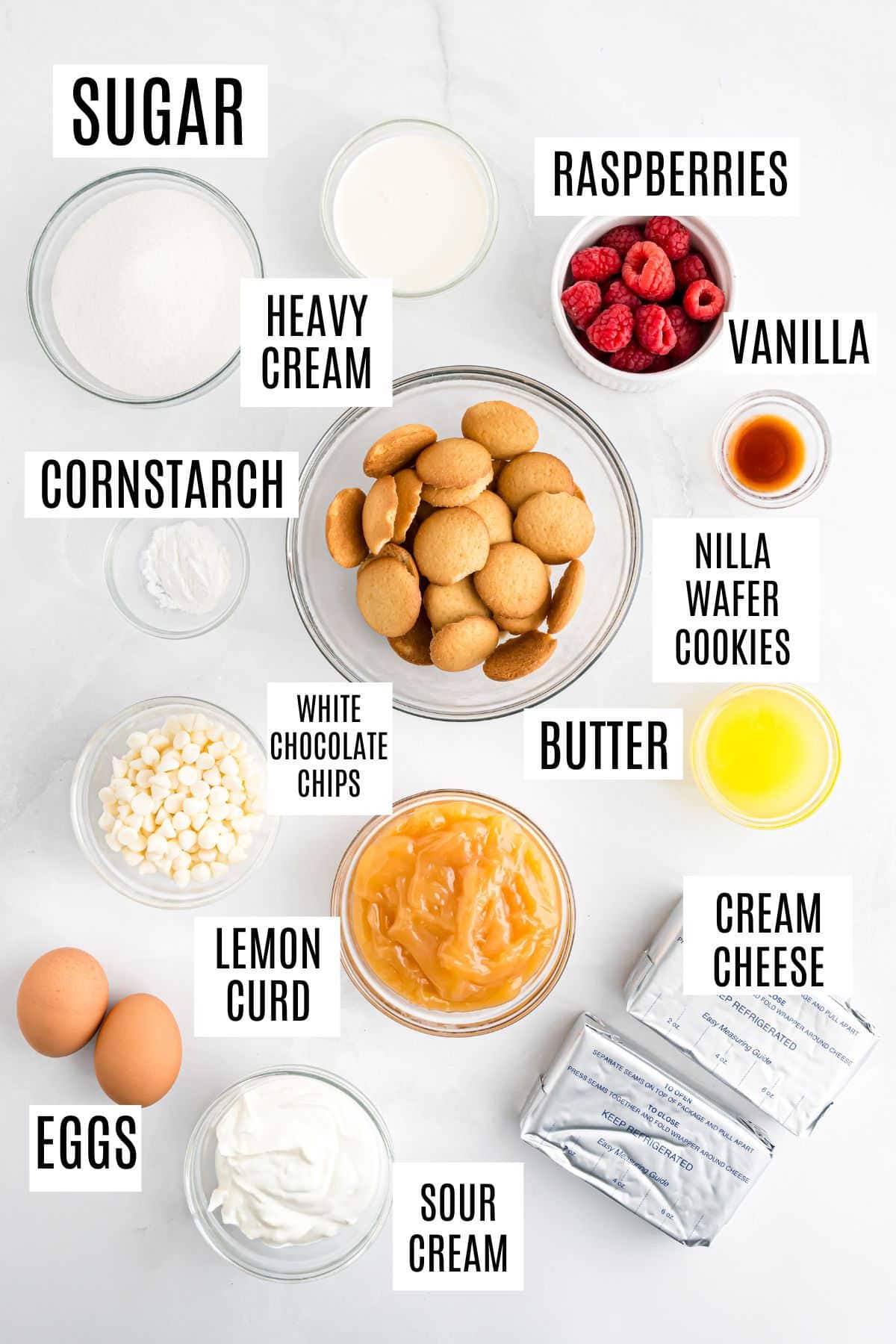 Labeled ingredients for baking lemon raspberry cheesecake bites: sugar, creams, raspberries, vanilla, cookies, chips, butter, lemon curd, eggs, and cheese.