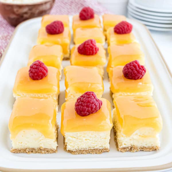 Rows of lemon raspberry cheesecake bites topped with fresh raspberries, arranged neatly on a white tray.