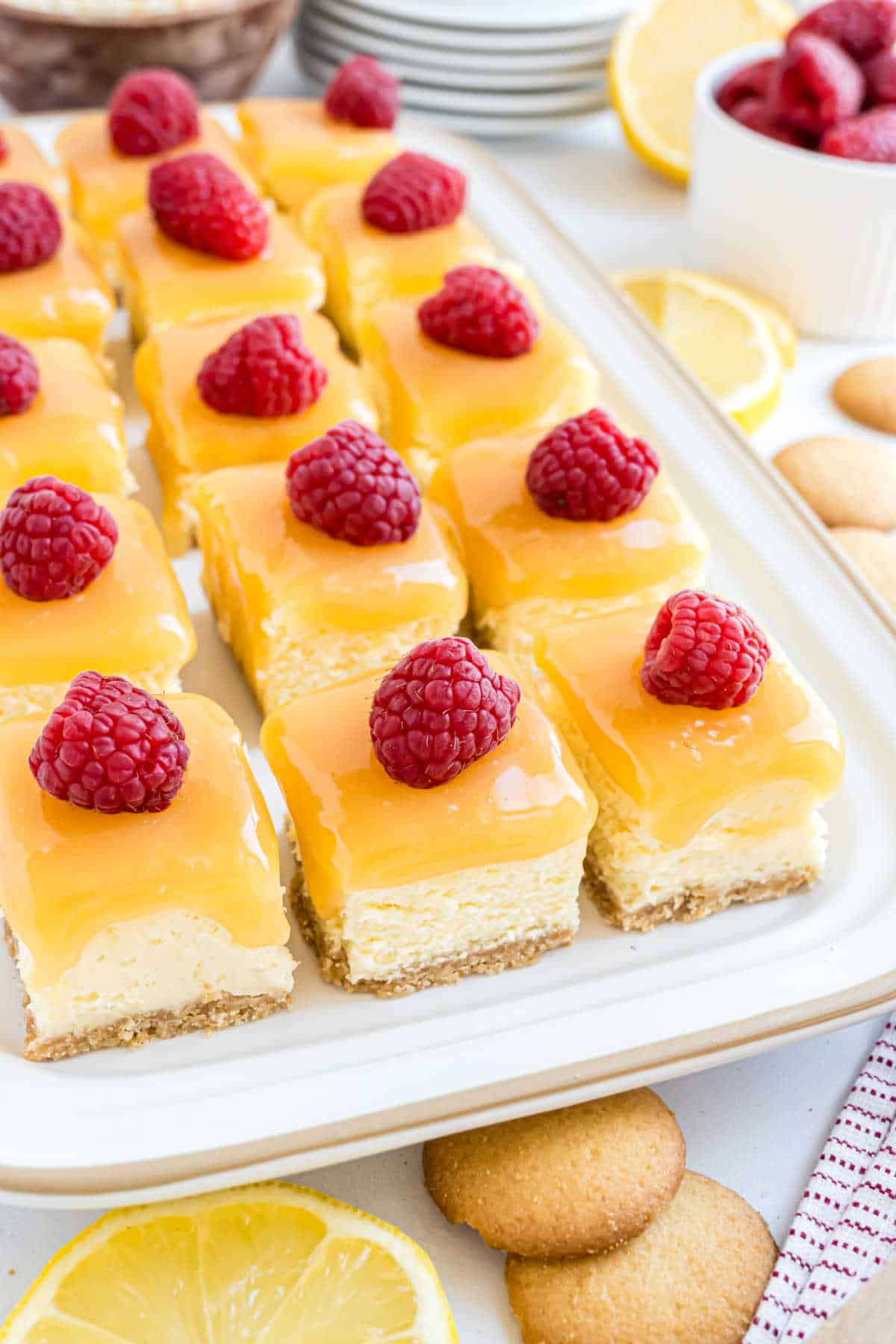Lemon raspberry cheesecake bites topped with lemon glaze and fresh raspberries, arranged on a white serving platter.