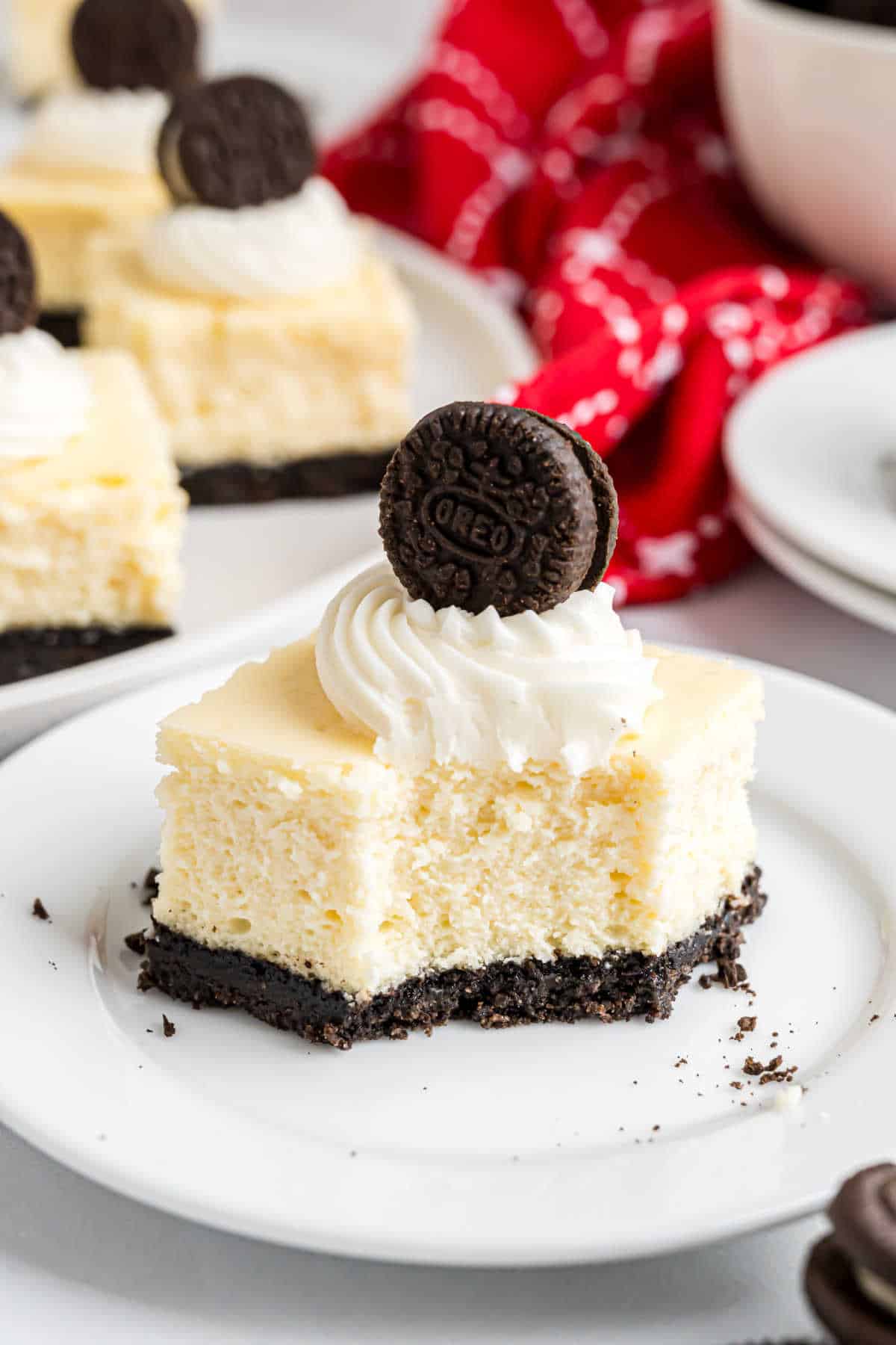 An Oreo cheesecake bite bar with an Oreo crust, topped with whipped cream and a mini Oreo cookie, served on a white plate.