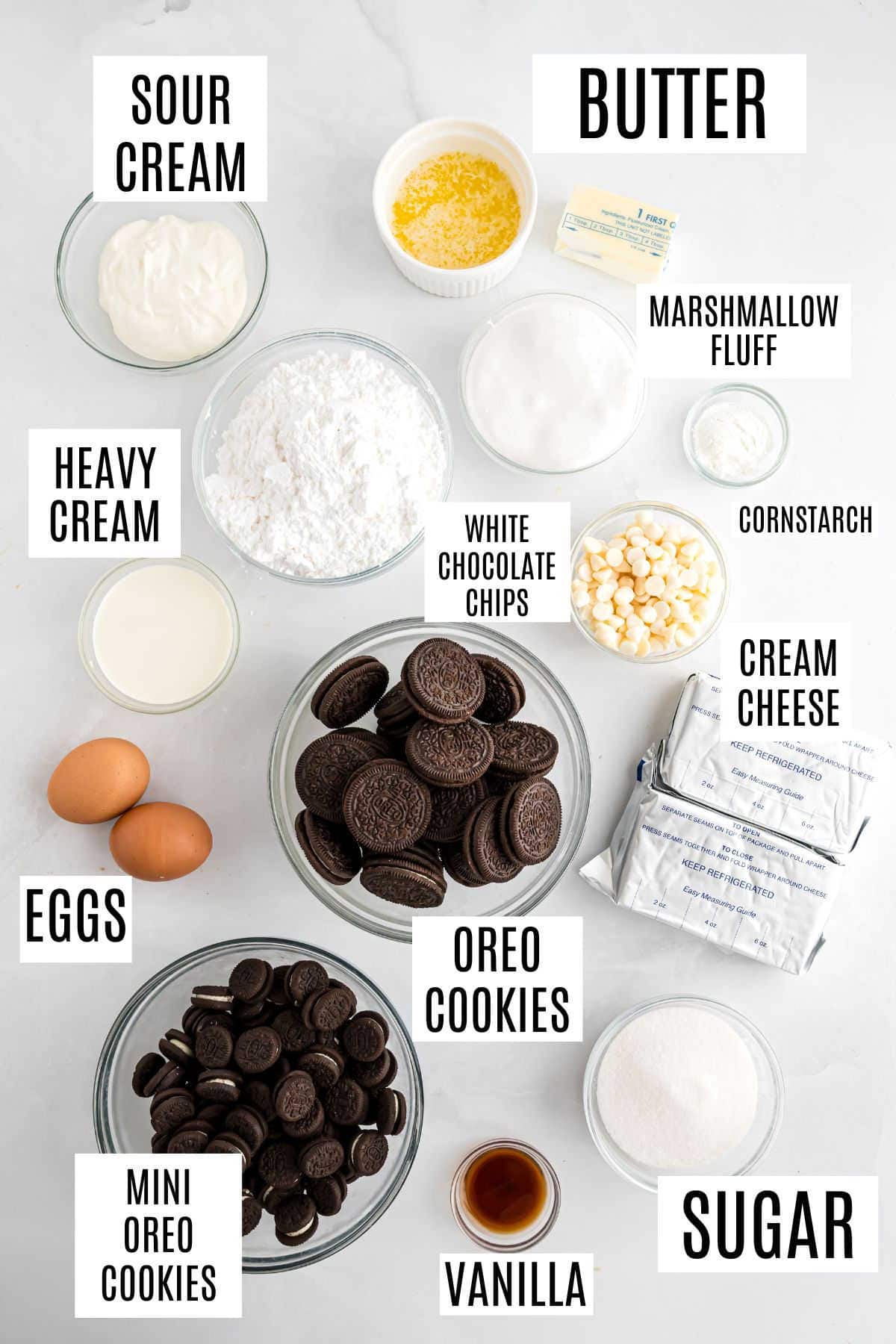 Various ingredients in bowls and plates labeled: sour cream, butter, Oreo cookies, eggs, sugar, and more—everything you need to make delicious Oreo cheesecake bites.