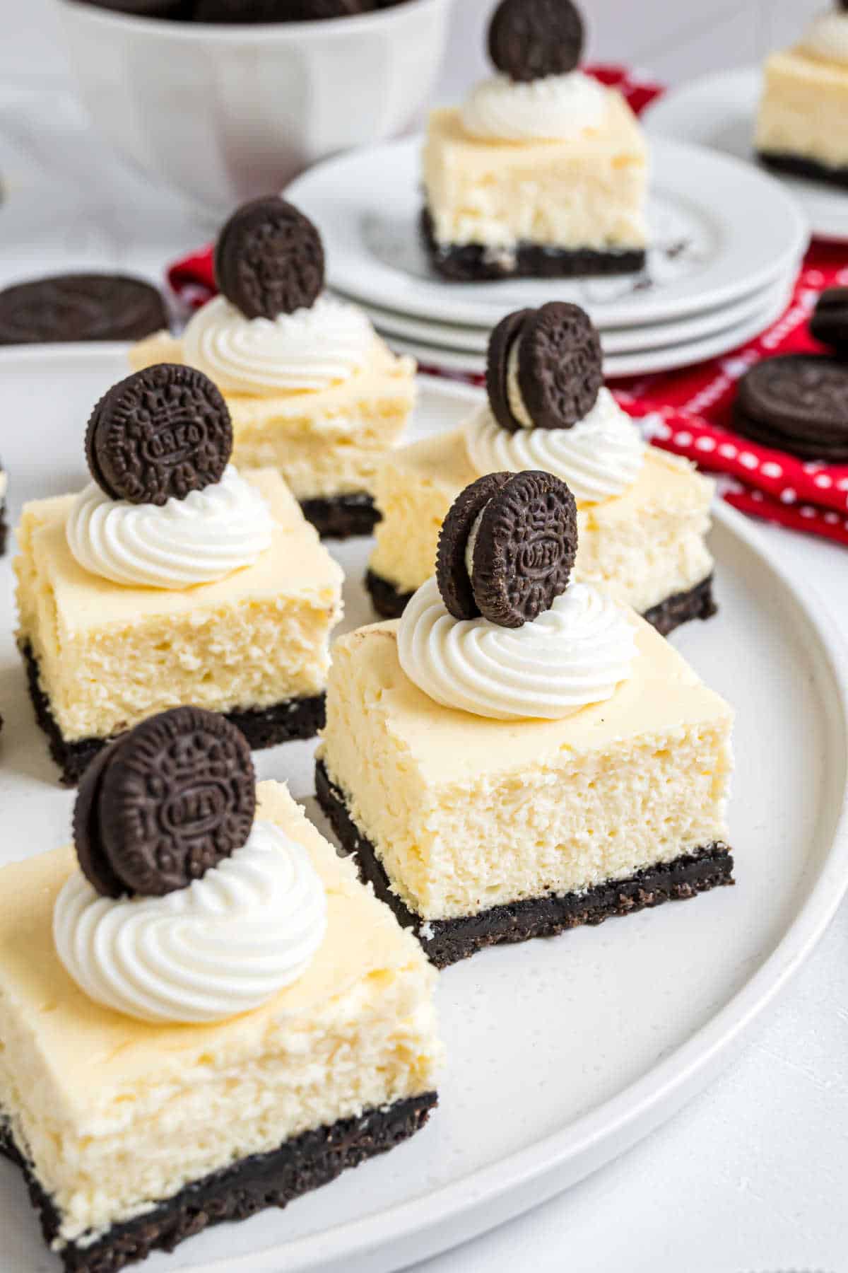Cheesecake bars with Oreo crust, topped with whipped cream and mini Oreo cookies, served on a white plate—these delightful Oreo cheesecake bites are perfect for any sweet craving.