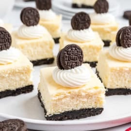 Oreo cheesecake bites featuring squares of creamy cheesecake on an Oreo cookie crust, topped with whipped cream and a mini Oreo cookie.