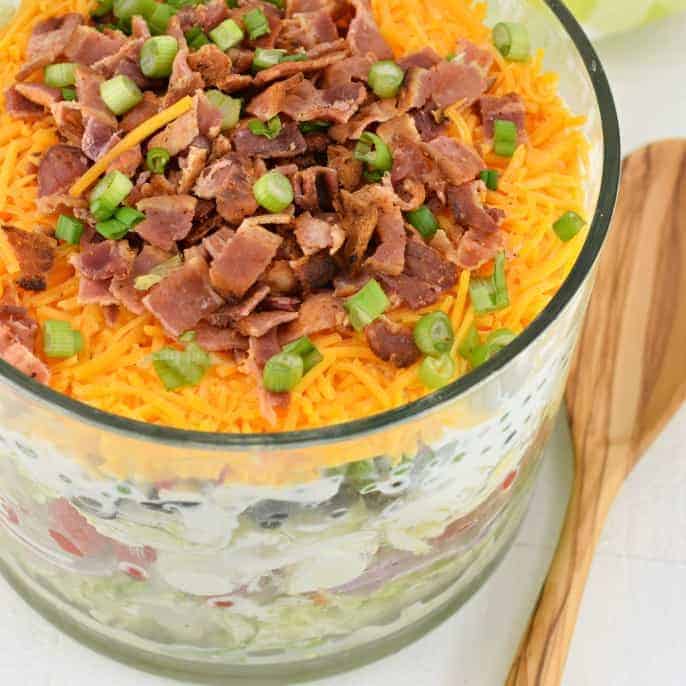 7 layer salad topped with cheese, bacon, and onion.