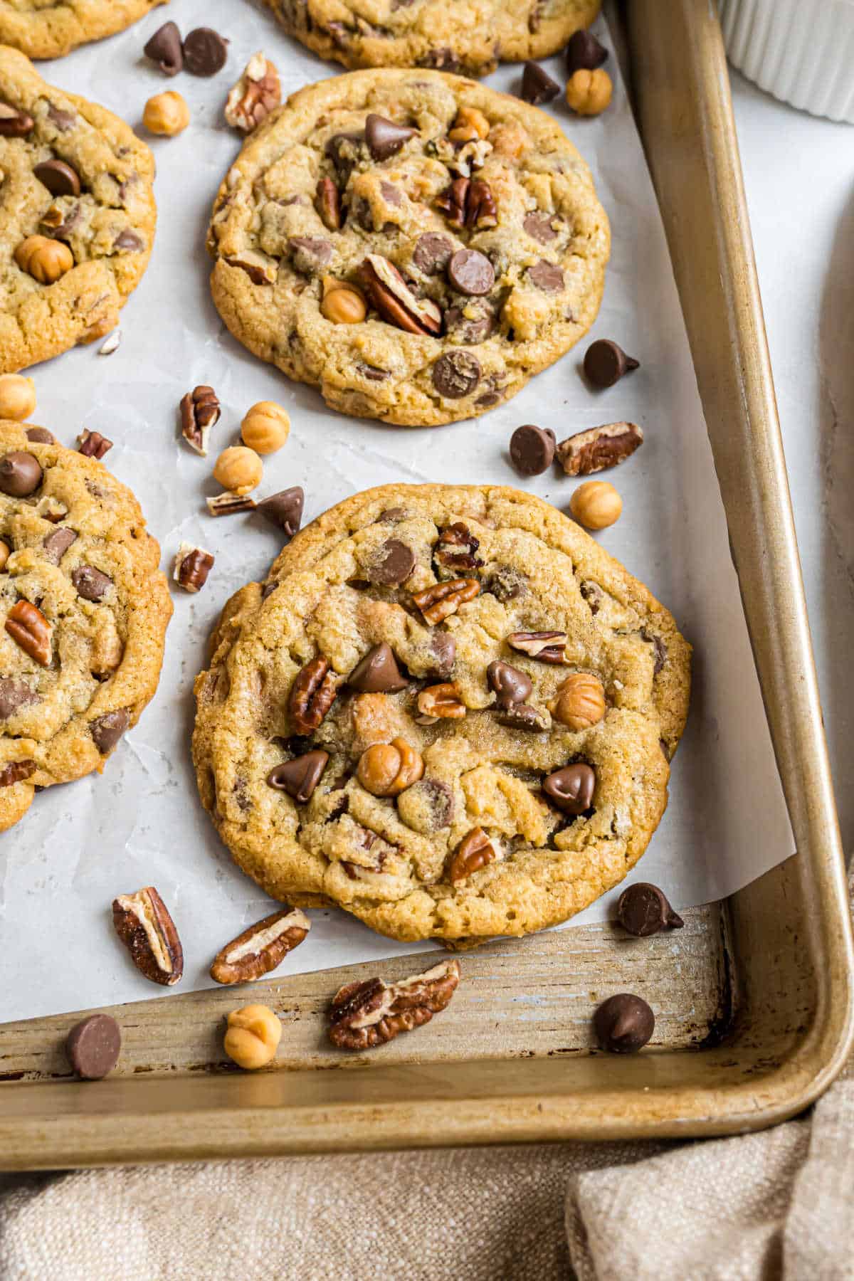 Caramel pecan chocolate chip cookies with butterscotch chips rest on a baking sheet lined with parchment paper.