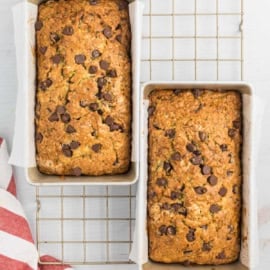 Two loaves of freshly baked chocolate chip zucchini bread in pans rest on a cooling rack, shot from above.
