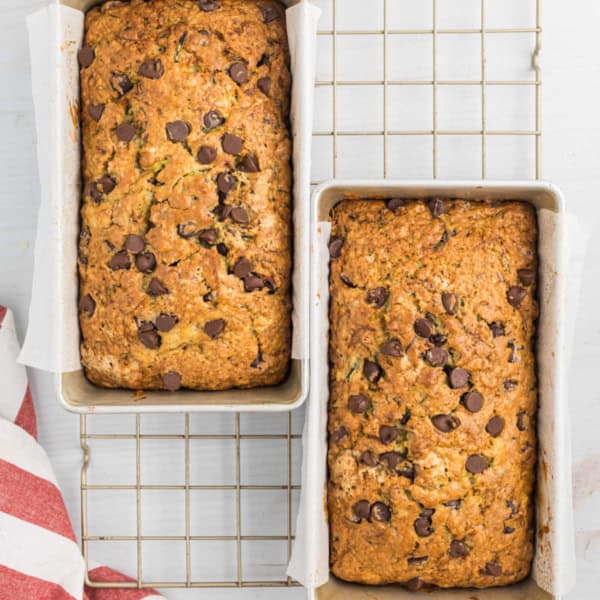 Two loaves of freshly baked chocolate chip zucchini bread in pans rest on a cooling rack, shot from above.