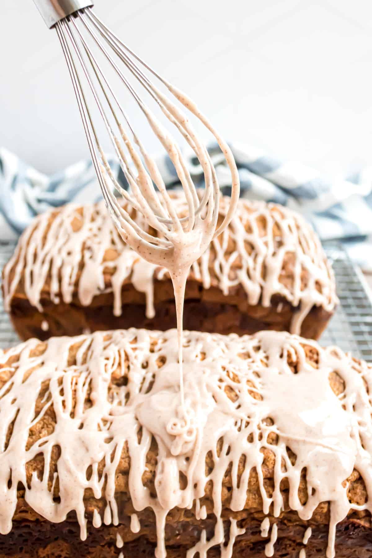 Cinnamon icing drizzling off a whisk onto zucchini bread.