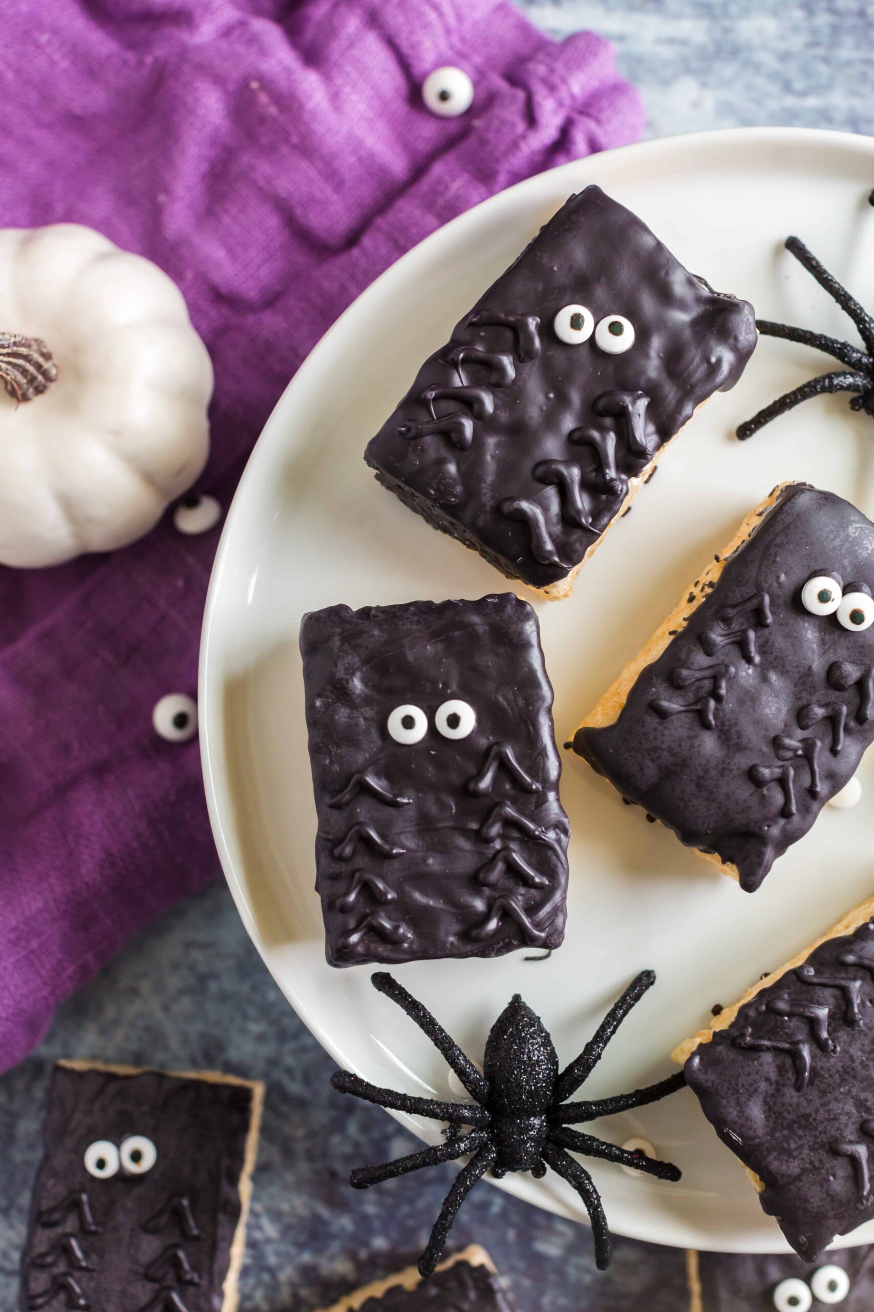 Plate with rice krispie treats decorated with chocolate and candy eyes to resemble spiders.