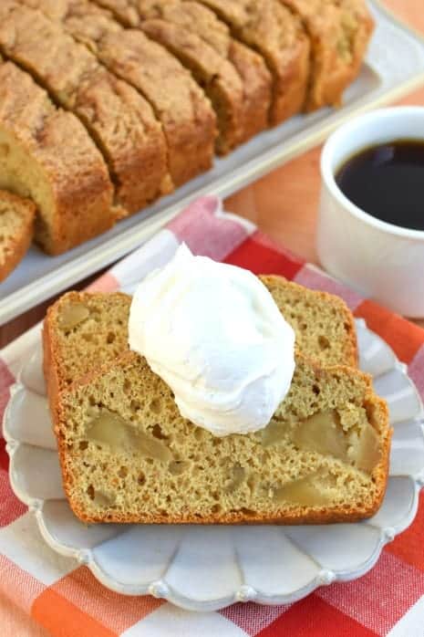 Two slices of Apple Bread topped with ice cream and served with hot cup of coffee. Red/orange linen underneath.