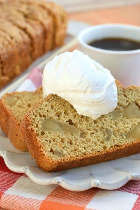 Two slices of apple bread on a white plate dolloped with whipped cream.