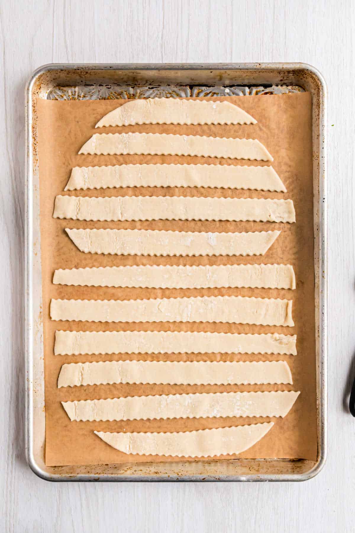 Pie crust on a parchment paper baking sheet cut into strips.