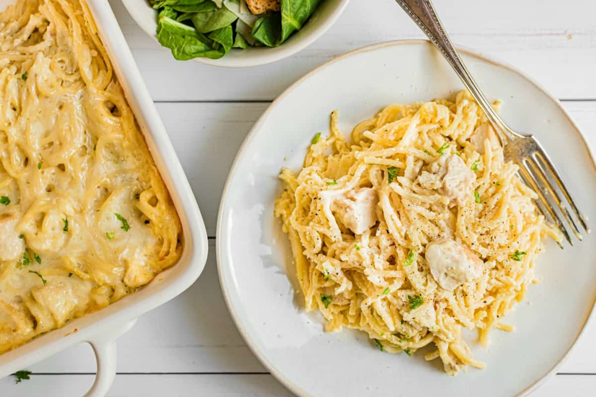 Chicken tetrazzini on a white dinner plate, silver fork, and 13x9 dish in background.