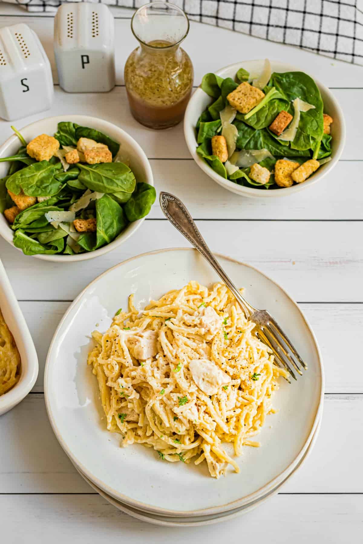 Chicken casserole served on a white dinner plate with two small side salads in background.