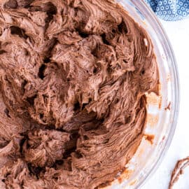 Chocolate buttercream frosting in a clear glass mixing bowl.