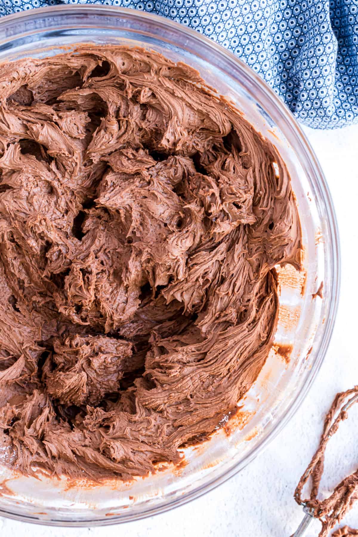 Chocolate buttercream frosting in a clear glass mixing bowl.