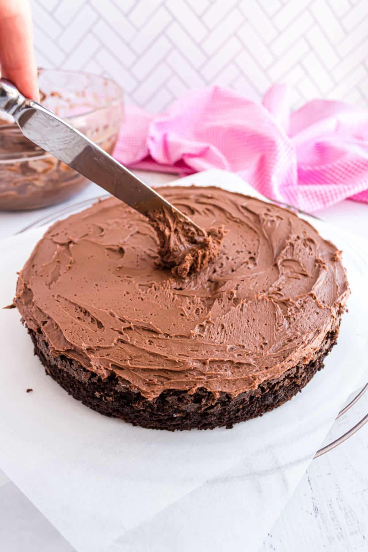 Chocolate frosting being added to a chocolate layer cake.