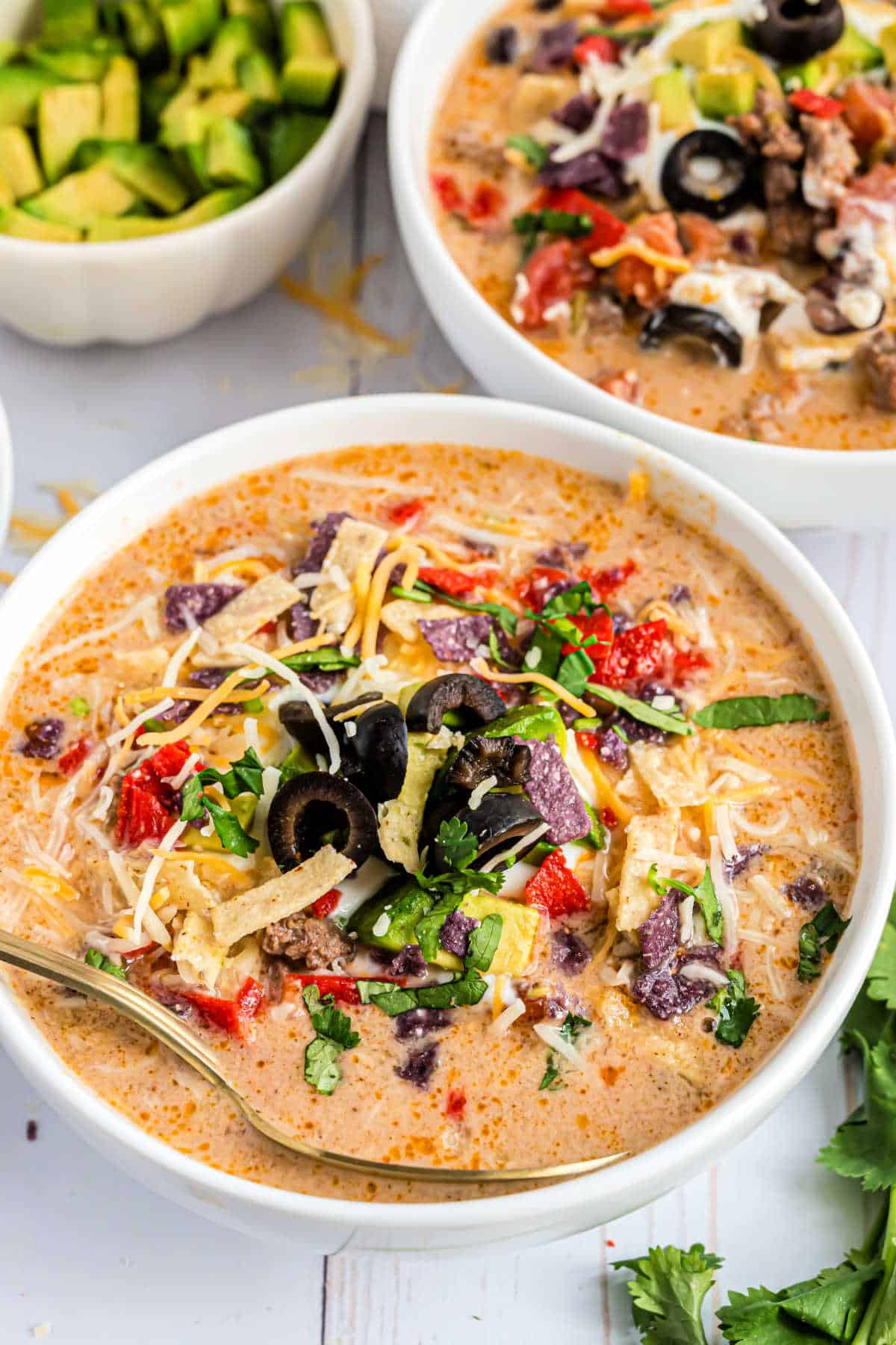 Bowl of taco soup topped with sour cream, tortilla chips, and avocados.