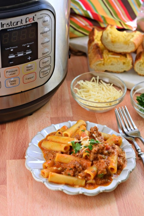 Ziti on a plate with instant pot and garlic bread in background.