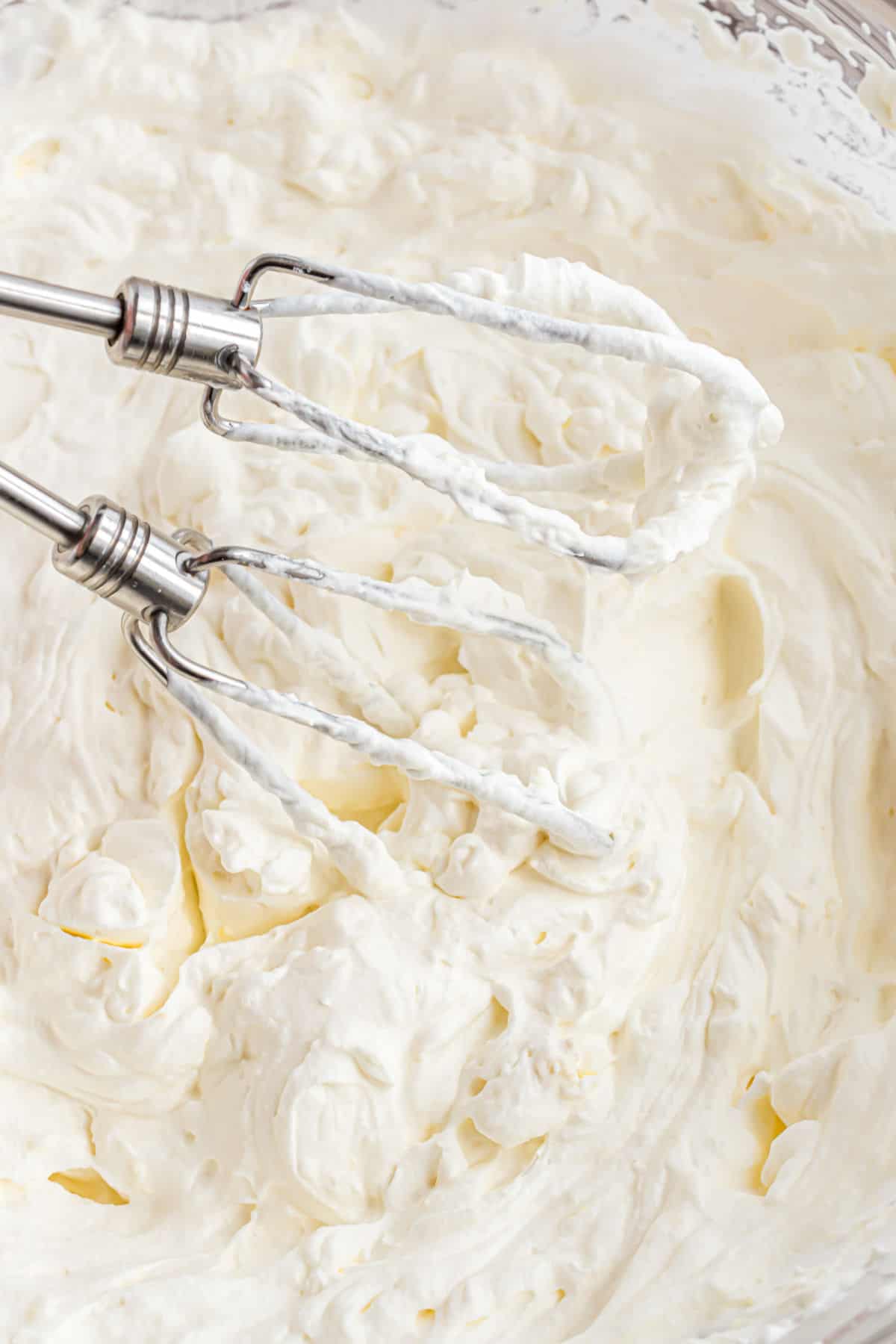 Lemon whipped cream in a glass bowl with electric beaters.