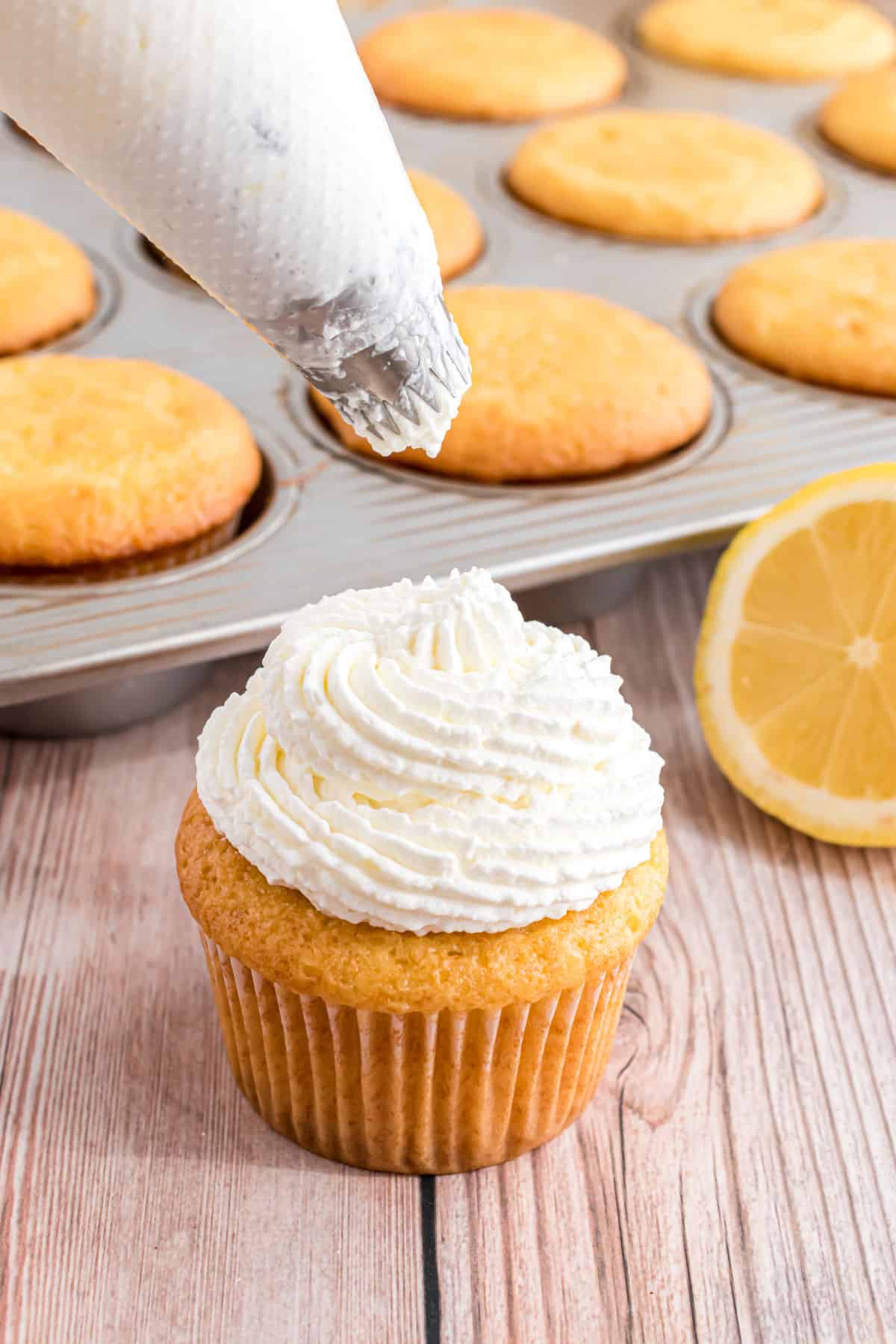 Lemon whipped cream being piped onto a cupcake.