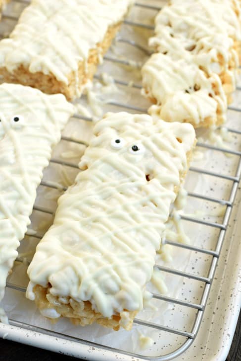 Mummy rice krispie treat dunked in white chocolate and setting on a wire rack to dry.