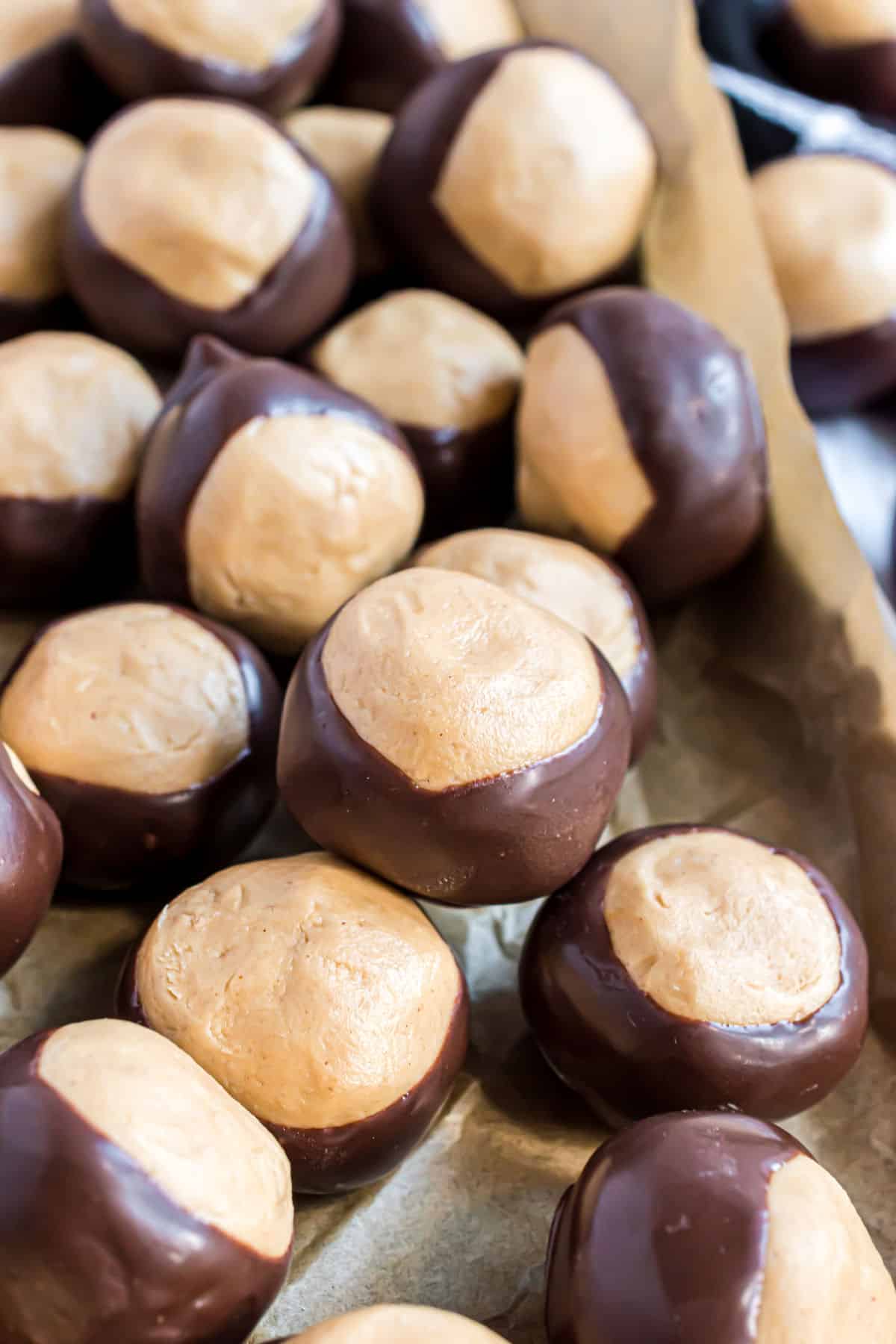 Buckeyes dipped in chocolate and stacked on parchment paper cookie sheets.