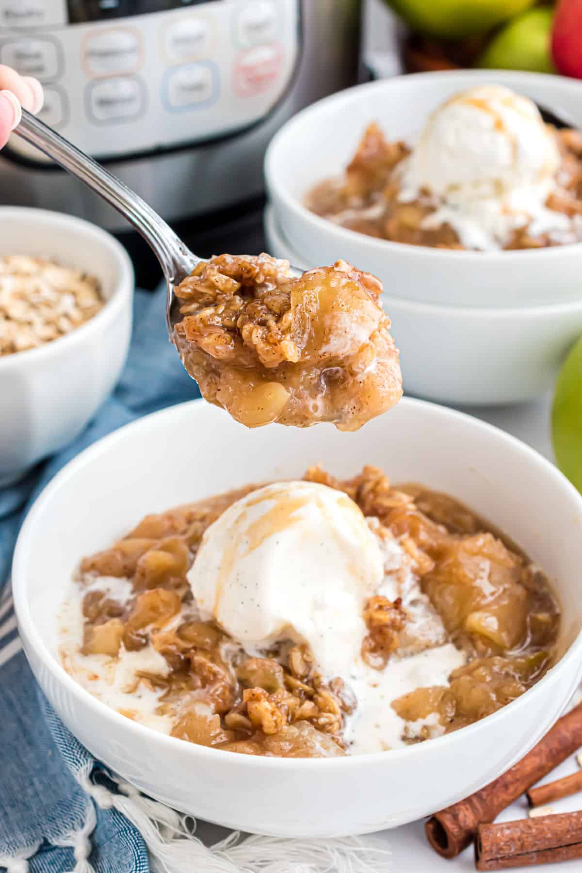 Spoon taking a bite of warm apple crisp with ice cream.