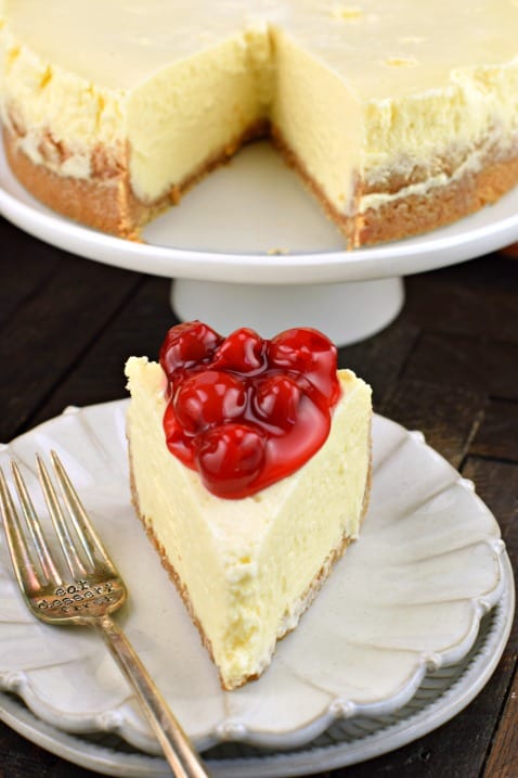 Slice of cheesecake on plate with whole cheesecake in background.