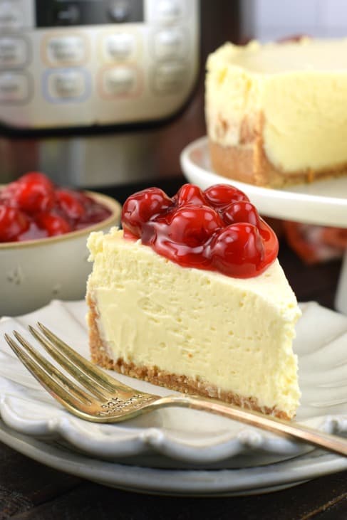 Slice of cheesecake with cherry pie filling on a small plate with fork.
