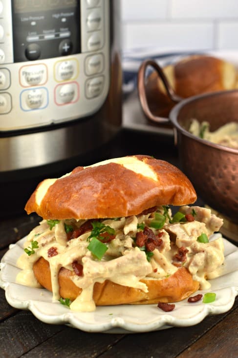 Crack chicken on a pretzel bun with instant pot in background.