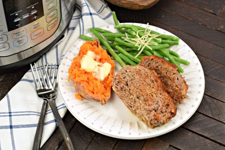 Meatloaf on a white plate with sweet potato, green beans, and instant pot in background.