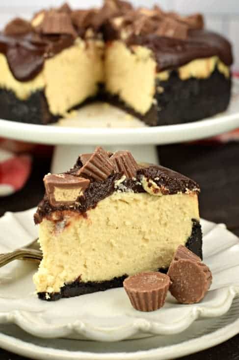 Big slice of Instant Pot Peanut Butter cheesecake covered in chocolate ganache and topped with Reese's peanut butter cups.