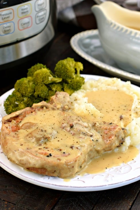 Pork chop and mashed potatoes covered in mushroom gravy on a white plate with a side of steamed broccoli.