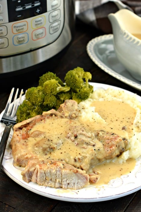 Pork chop with a piece cut to see the tender inside. Topped with mushroom gravy on a white plate and pressure cooker in background.