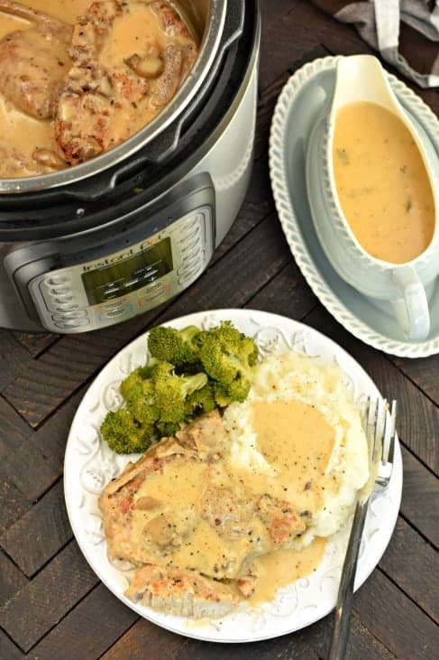 Pork chops, mashed potatoes and broccoli covered in mushroom gravy on a white plate. Gravy bowl and Instant Pot in background.