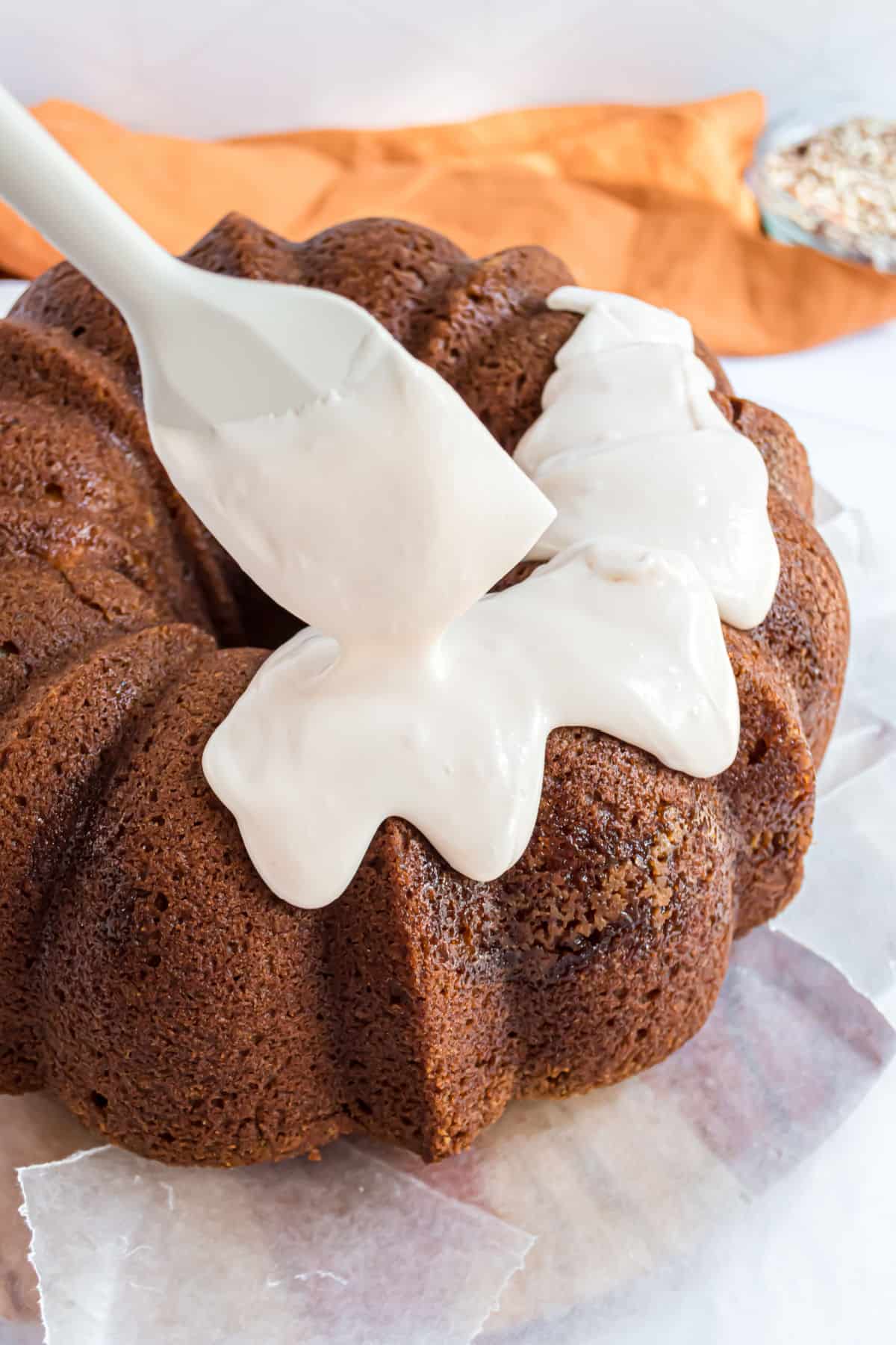 Thick icing being drizzled over the top of a pumpkin bundt cake.