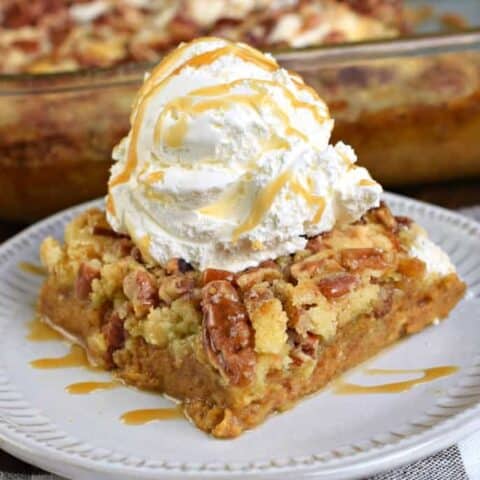 Slice of pumpkin dump cake on a plate with vanilla ice cream and caramel sauce.