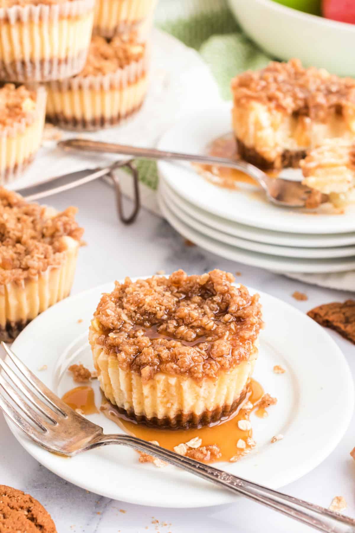 Streusel topped apple cheesecake with caramel sauce on a white plate with fork.