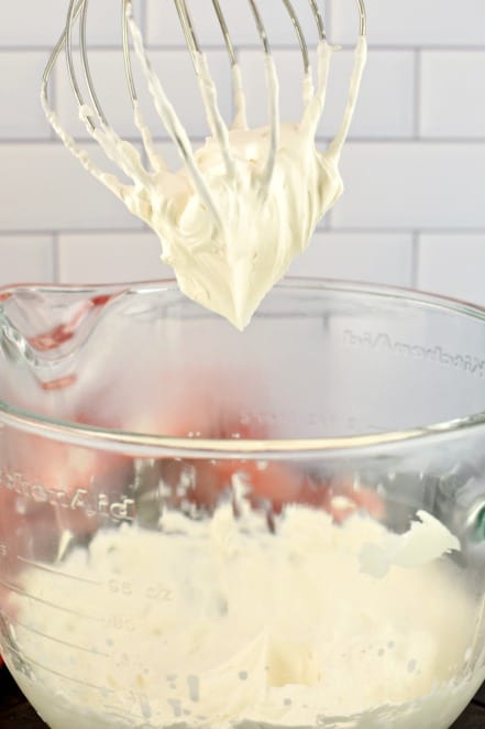 Clear glass mixing bowl with whisk showing thick whipped cream.