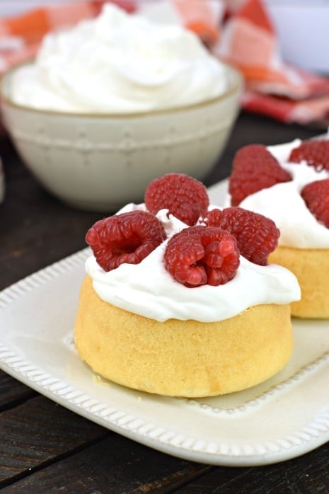 Sponge cakes topped with whipped cream and fresh raspberries on a white serving platter.